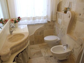 A bathroom with a sink, toilet, bidet, and a window with curtains.