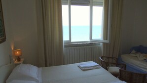 Un dormitorio con cama, una silla, una mesa con lámpara y vista al mar a través de una ventana.