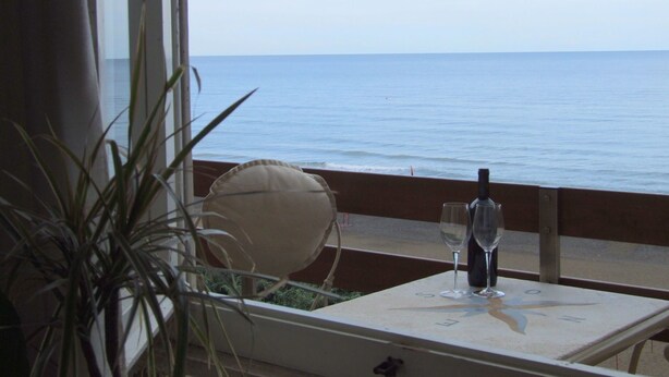 Una mesa con una botella y dos vasos, con vistas al mar.