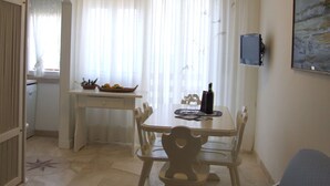 Un comedor con una mesa, sillas, una mesita auxiliar con una cesta de frutas y una botella de vino.