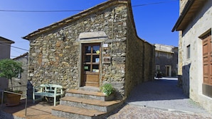 Un bâtiment en pierre avec une porte en bois, des marches menant à l’entrée et un banc à l’extérieur.