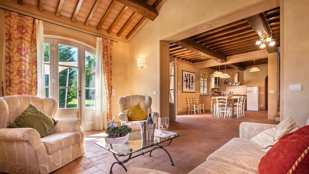 A spacious living room with a sofa, armchair, and a glass coffee table. There is a dining area with a table and chairs, and a kitchen visible in the background. - Beautiful private villa for 6 guests with private pool, A/C, WIFI, TV and veranda, close to Lucca (Capannori)