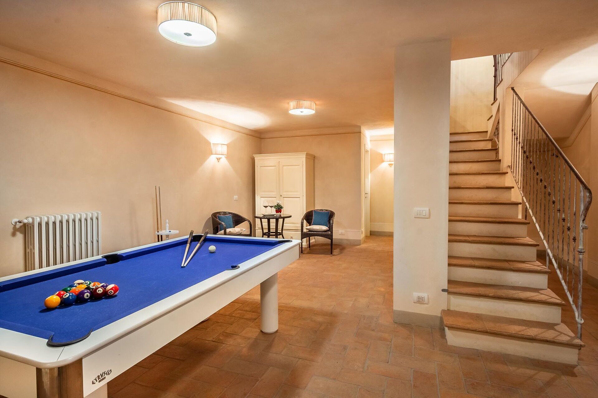 A pool table in a room with a staircase and a radiator.