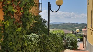 Un estrecho callejón con sendero de ladrillo, una farola y vistas a colinas distantes.