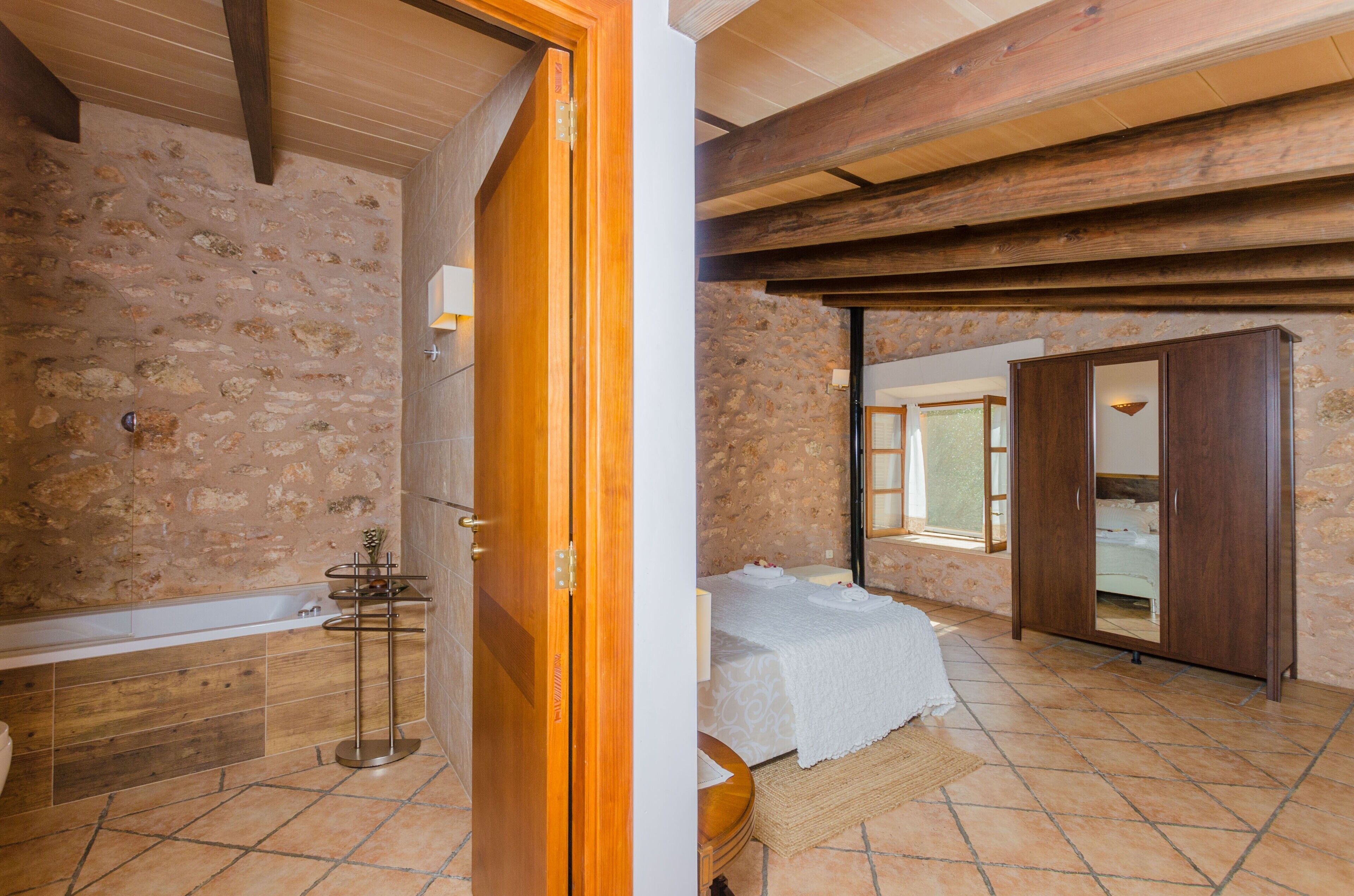 Une chambre à coucher avec un lit, une armoire en bois et une salle de bain dotée d’une baignoire et de murs carrelés.