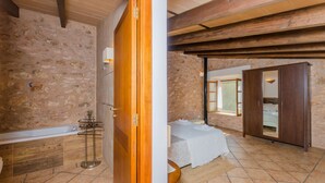A bedroom with a bed, wooden wardrobe, and a bathroom with a bathtub and tiled walls. - CAN FOSQUET - Beautiful traditional villa with private pool. Free WiFi. (Llucmajor)