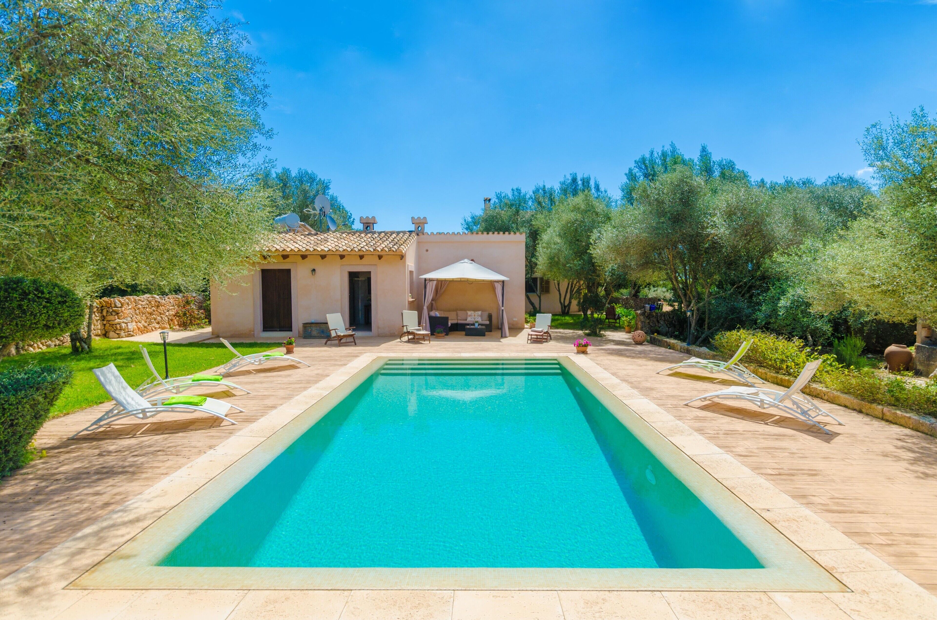 A rectangular swimming pool with lounge chairs and a covered seating area in a landscaped garden.