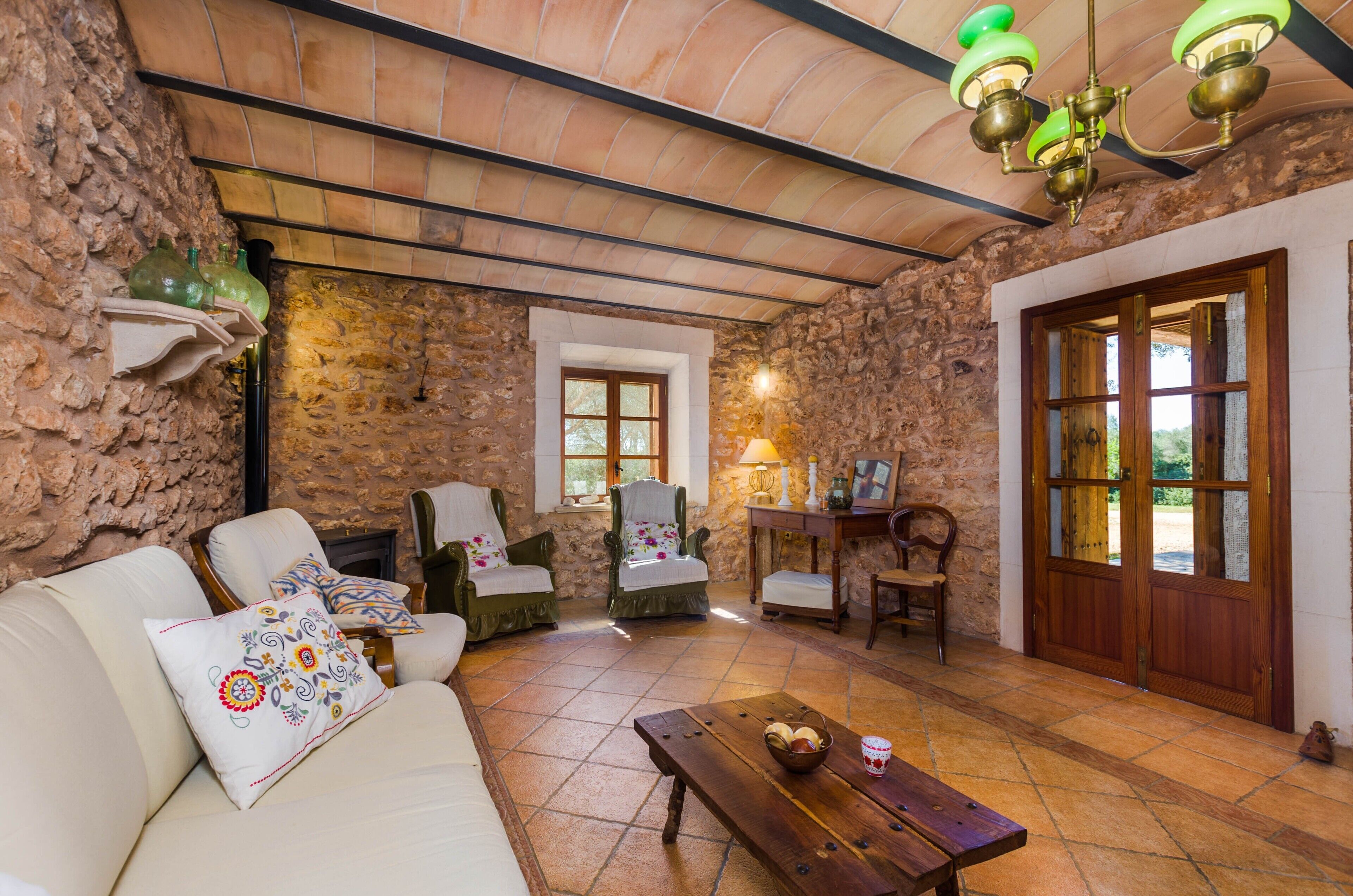 Una habitación rústica con paredes de piedra, techo de madera, un sofá con cojines estampados, una mesa de madera con una cesta y una puerta de madera con paneles de vidrio.