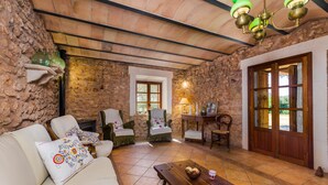 A rustic stone-walled room with a wooden ceiling, a sofa with patterned cushions, a wooden table with a basket, and a wooden door with glass panels. - CAN FOSQUET - Beautiful traditional villa with private pool. Free WiFi. (Llucmajor)