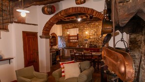 Een rustiek interieur met een stenen boog die leidt naar een keuken, een eethoek met houten meubels, en een zithoek met een bank en stoelen.