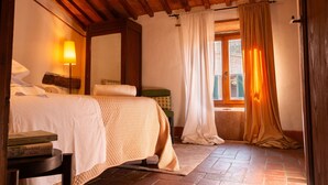 Een knus slaapkamer met een houten plafond, een bed met een gewatteerde spreideken, een nachtkastje met boeken en een raam met gordijnen.