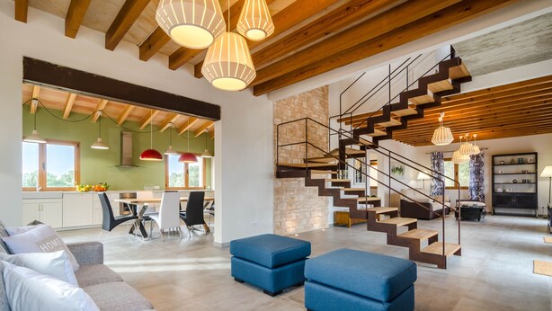 A spacious living area with a modern staircase, a dining area, and a kitchen with large windows.
