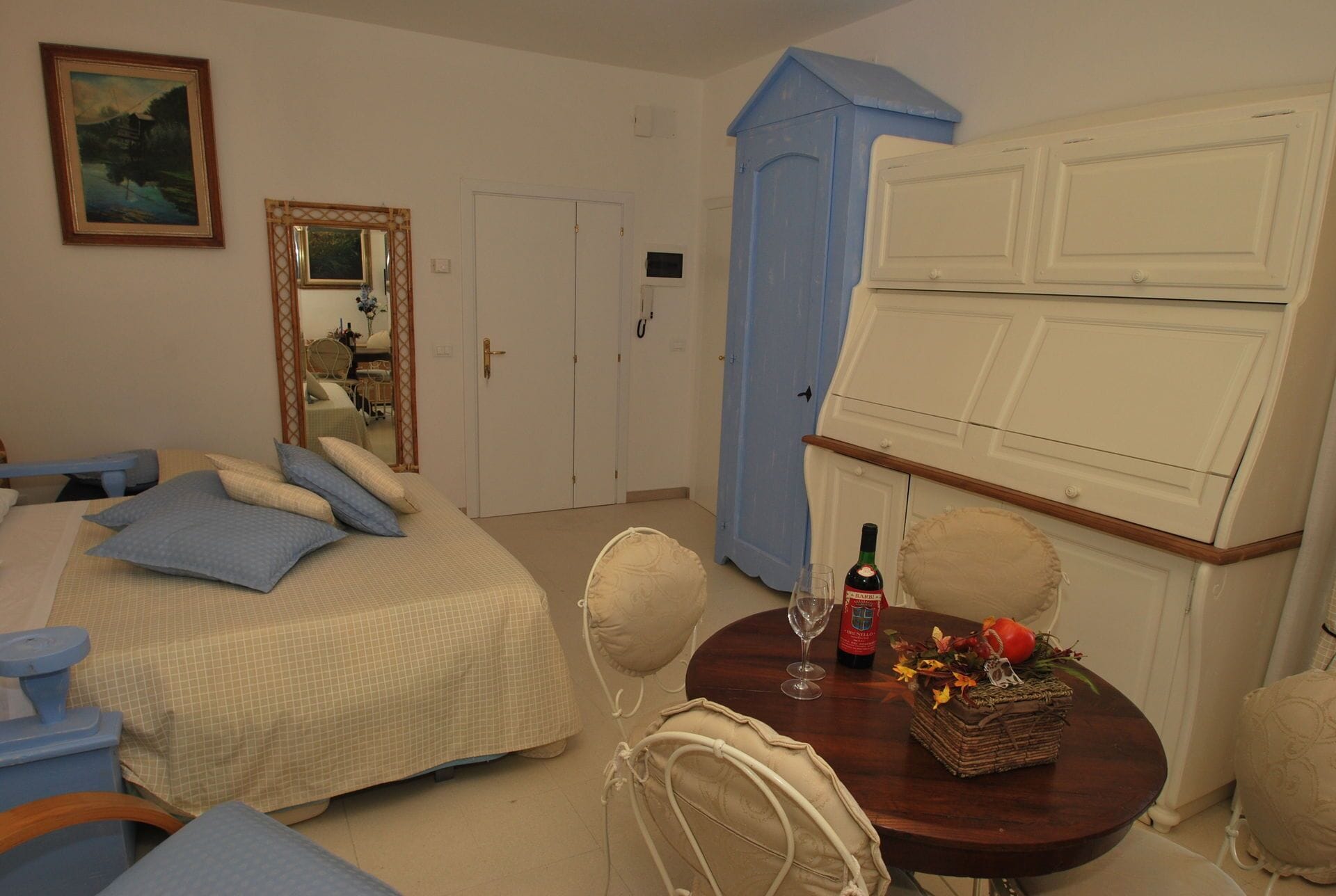 A bedroom with a bed, bedside table, and a small round table with a bottle and glass.