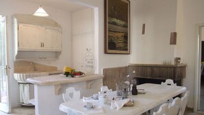 Un comedor con una mesa y sillas blancas, una cocina con armarios blancos y un cuadro en la pared.