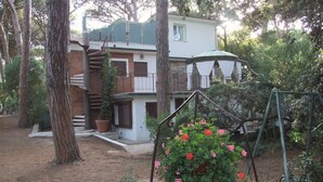 Una casa de dos pisos con un balcón, rodeada de árboles y un columpio.
