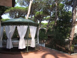 Un belvédère agrémenté de rideaux blancs, d’un banc et d’une terrasse carrelée.