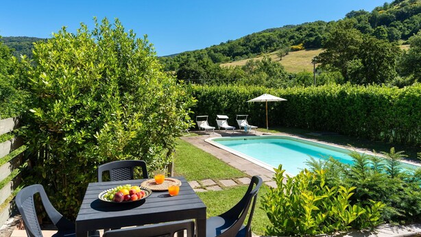 Un área junto a la piscina con una mesa para dos, una piscina y sillones de descanso.