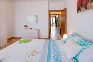 Ein Schlafzimmer mit Bett, Schminktisch, Spiegel und einer Tür zu einem weiteren Raum.