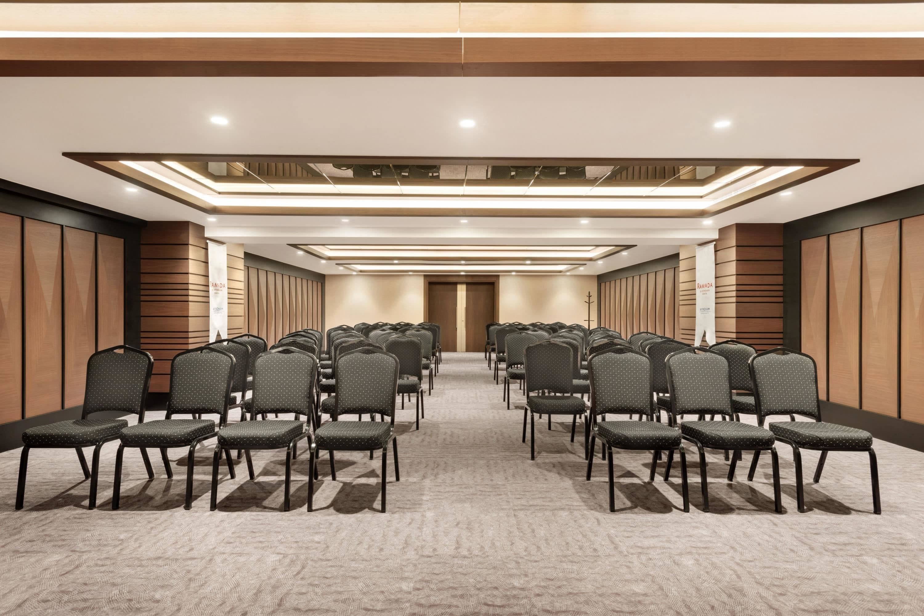 Un salón de conferencias con filas de sillas, piso alfombrado y paneles de madera.
