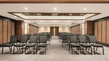 Un salón de conferencias con filas de sillas, piso alfombrado y paneles de madera.