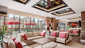 Un moderno vestíbulo de hotel con un sofá, sillones y una mesa de centro. Amplias ventanas ofrecen vistas al exterior.
