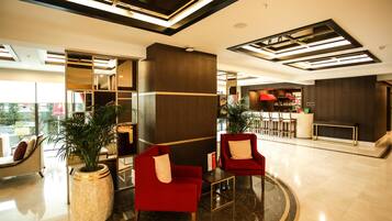 A modern lobby with red armchairs, a marble floor, and a bar area.