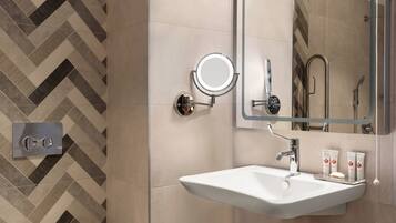 A modern bathroom with a white sink, a round mirror, and a shower area.