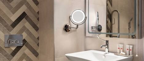 A modern bathroom with a white sink, a round mirror, and a shower area.