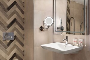 Un baño moderno con un lavamanos blanco, un espejo redondo y una zona de ducha.