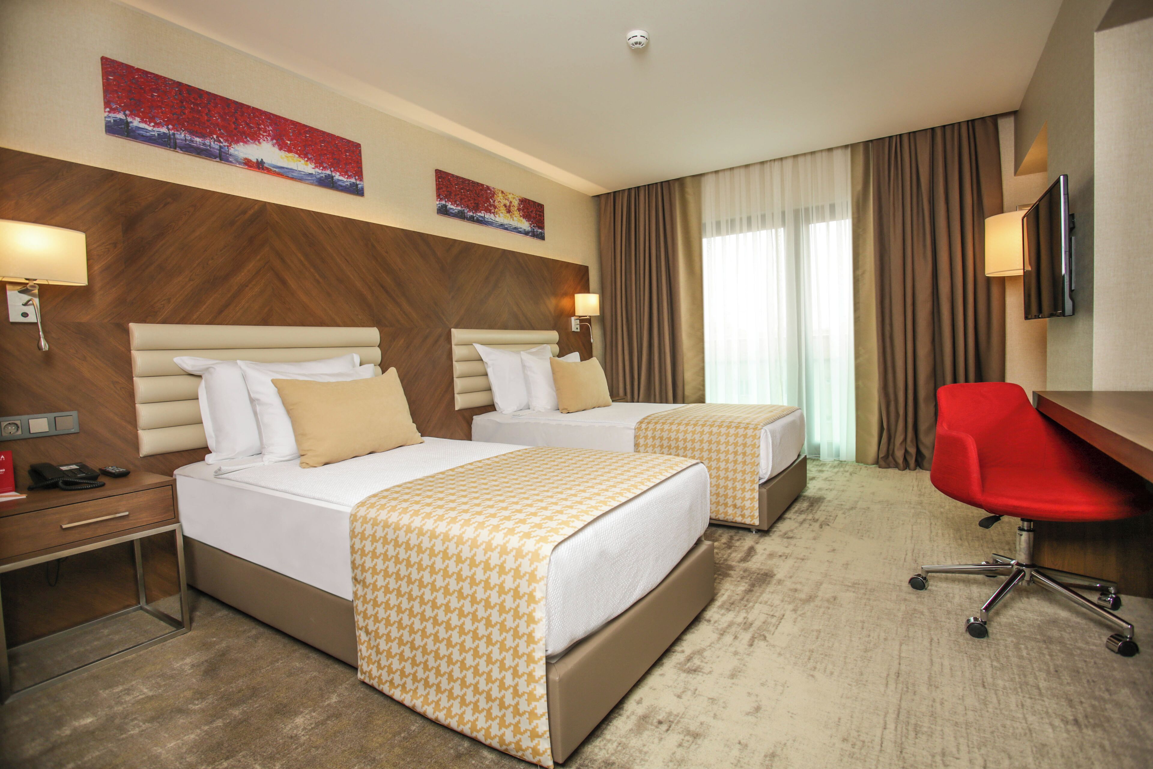 Habitación de hotel con dos camas, un escritorio, una silla de oficina roja y un televisor.