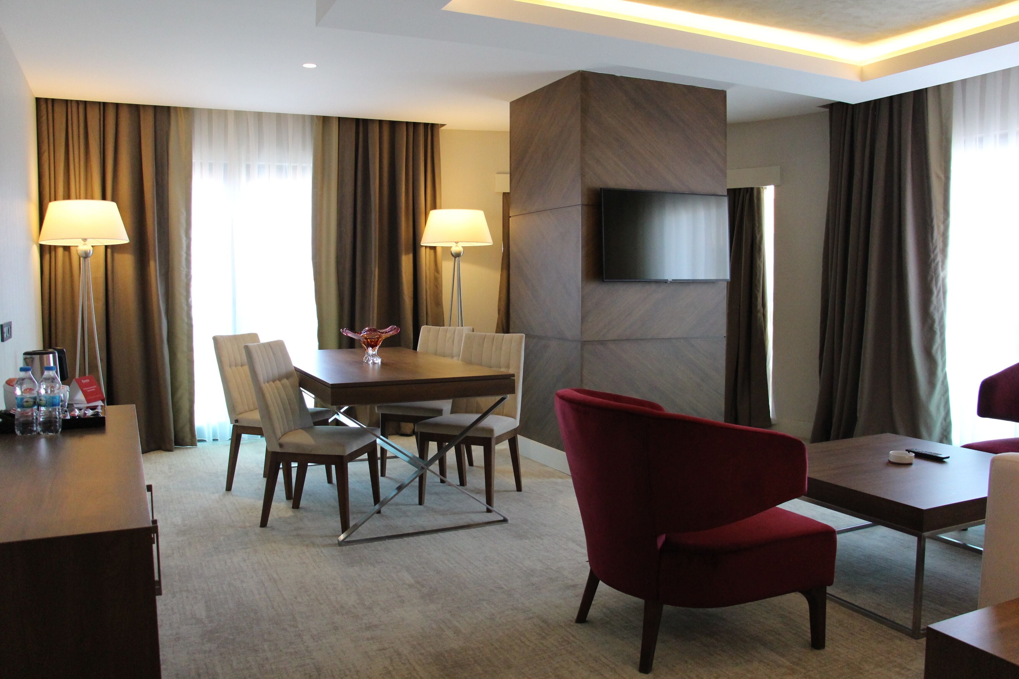 A hotel room with a dining area, a TV mounted on the wall, and a red chair.