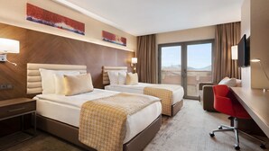Una habitación de hotel con dos camas, un escritorio, una silla y un ventanal amplio.