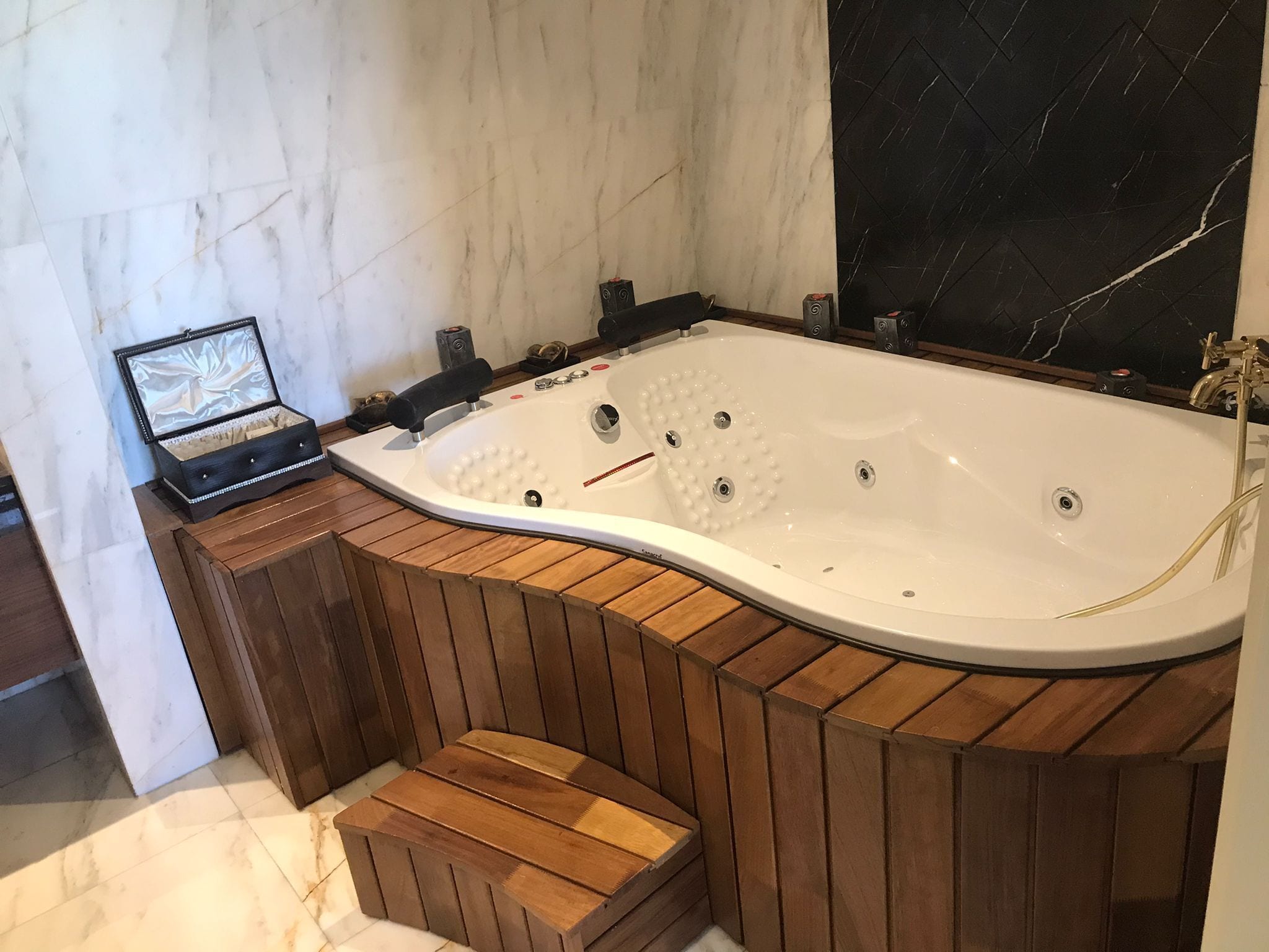 A modern bathroom with a freestanding bathtub, wooden paneling, marble walls, and a black tiled backsplash.