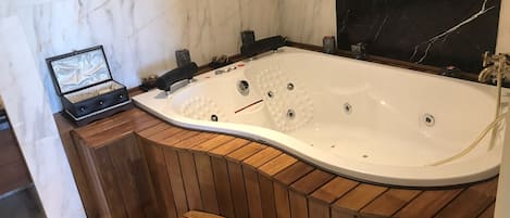 Un baño moderno con una bañera independiente, paneles de madera, paredes de mármol y un salpicadero de azulejos negros.