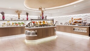 Un área de buffet moderna y bien iluminada con diversas opciones de comida, como frutas, ensaladas y pasteles.