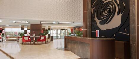 A hotel lobby with a reception desk, seating area, and a large wall art piece.