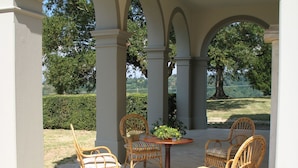 A covered patio area with wicker chairs and a round table, surrounded by white columns.