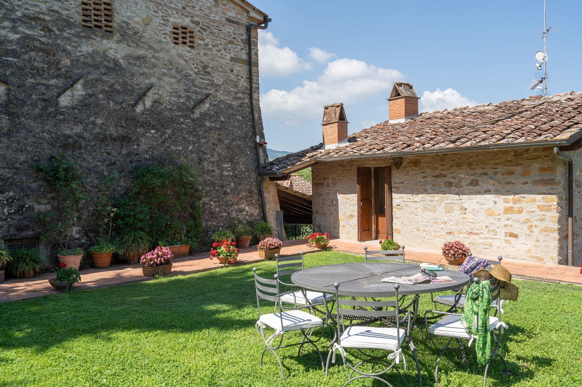 A stone building with a tiled roof, a grassy yard, and a metal table with chairs.
