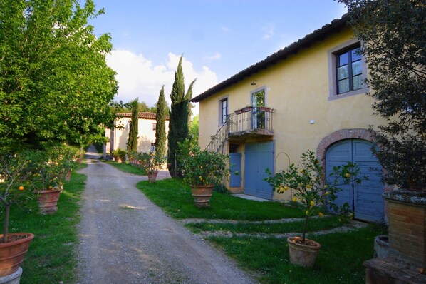 A narrow gravel path leading to a yellow building with a blue door and a balcony. - Beautiful apartment in villa with WIFI, pool, TV, patio and panoramic view, close to San Gimignano (Poggibonsi)