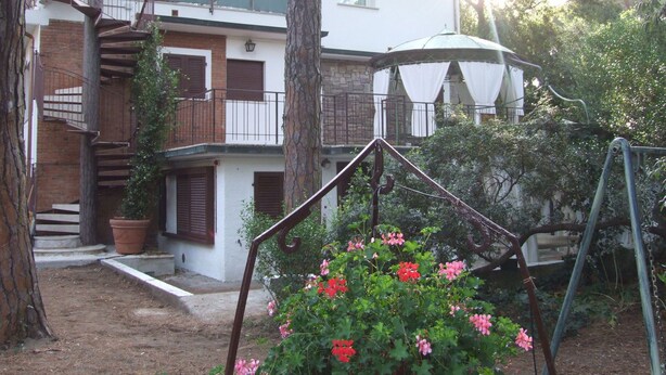 Ein zweistöckiges Gebäude mit Balkon, einer Treppe und einer Schaukel im Garten.