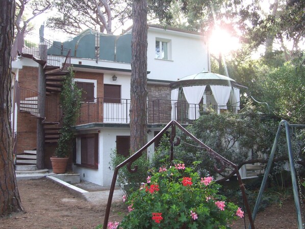 A two-story building with a balcony, a staircase, and a swing set in the garden.