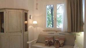 Ein Zimmer mit beiger Couch, einem Holzschrank, einem Fenster mit Vorhängen und einer Wandlampe.