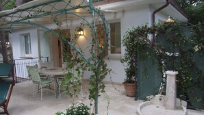 Eine Terrasse mit Tisch und Stühlen, einem Topfpflanzen und einer Steinfontäne.