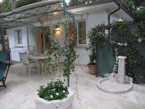 A patio with a table and chairs, a potted plant, and a stone fountain.