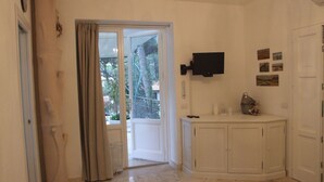Ein geräumiger Raum mit einer Schiebetür zu einem Balkon, einem an der Wand befestigten Flachbildfernseher und einer kleinen Kommode mit Dekoration.