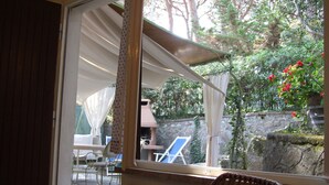 Une pièce donnant sur un patio, avec un fauteuil en osier et une table entourée de chaises à l’extérieur.