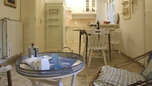 Une cuisine chaleureuse avec des meubles blancs, une table à manger entourée de chaises et un petit îlot central agrémenté d'une carafe et de verres.