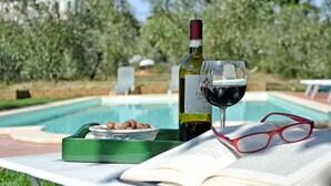 A poolside setting with a bottle of wine, a glass of red wine, a book, and a bowl of hazelnuts. - Stunning private villa for 6 guests with private pool, WIFI, A/C, TV and panoramic view (San Miniato)