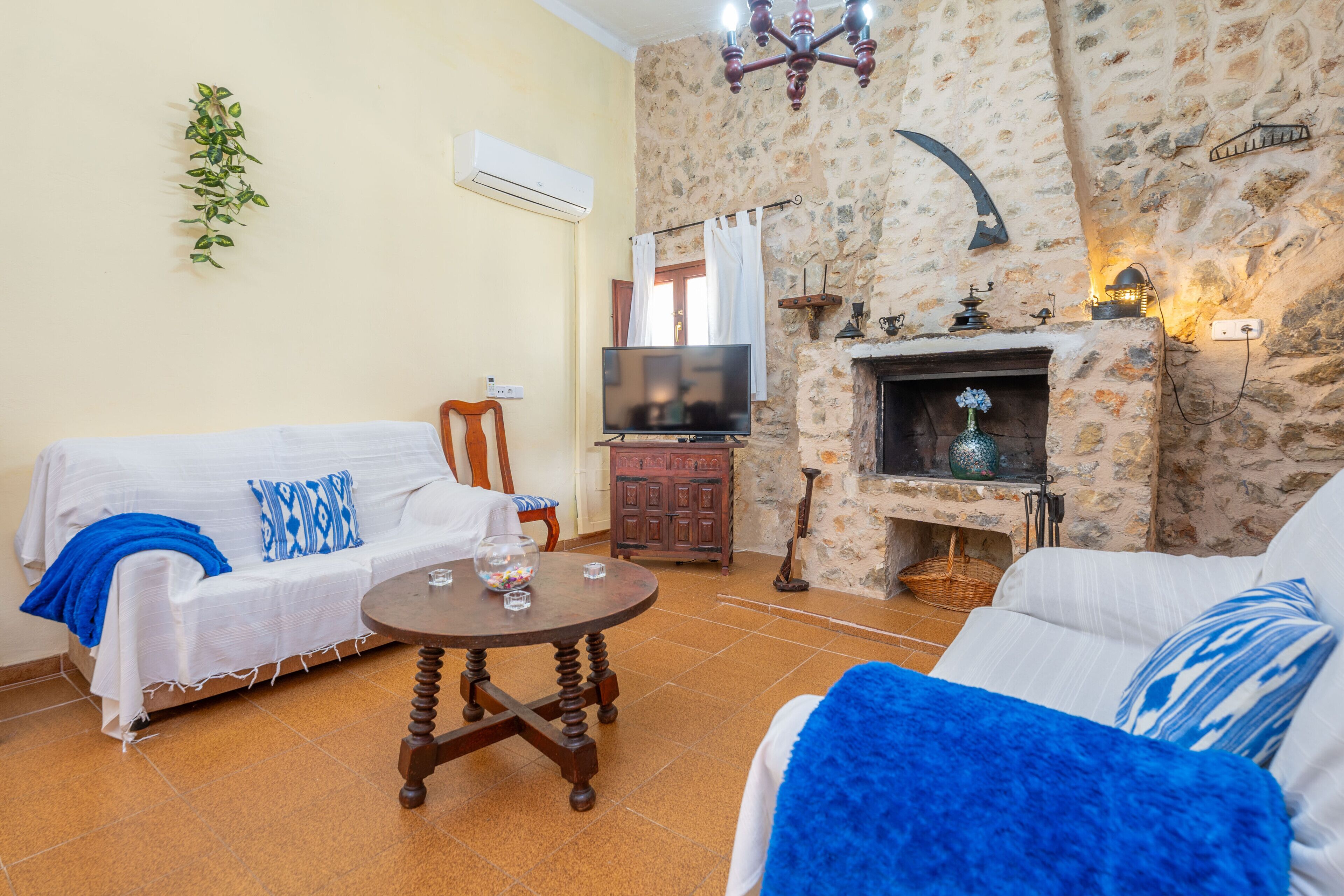 A living room with a stone fireplace, a television, and a sofa with blue and white cushions.