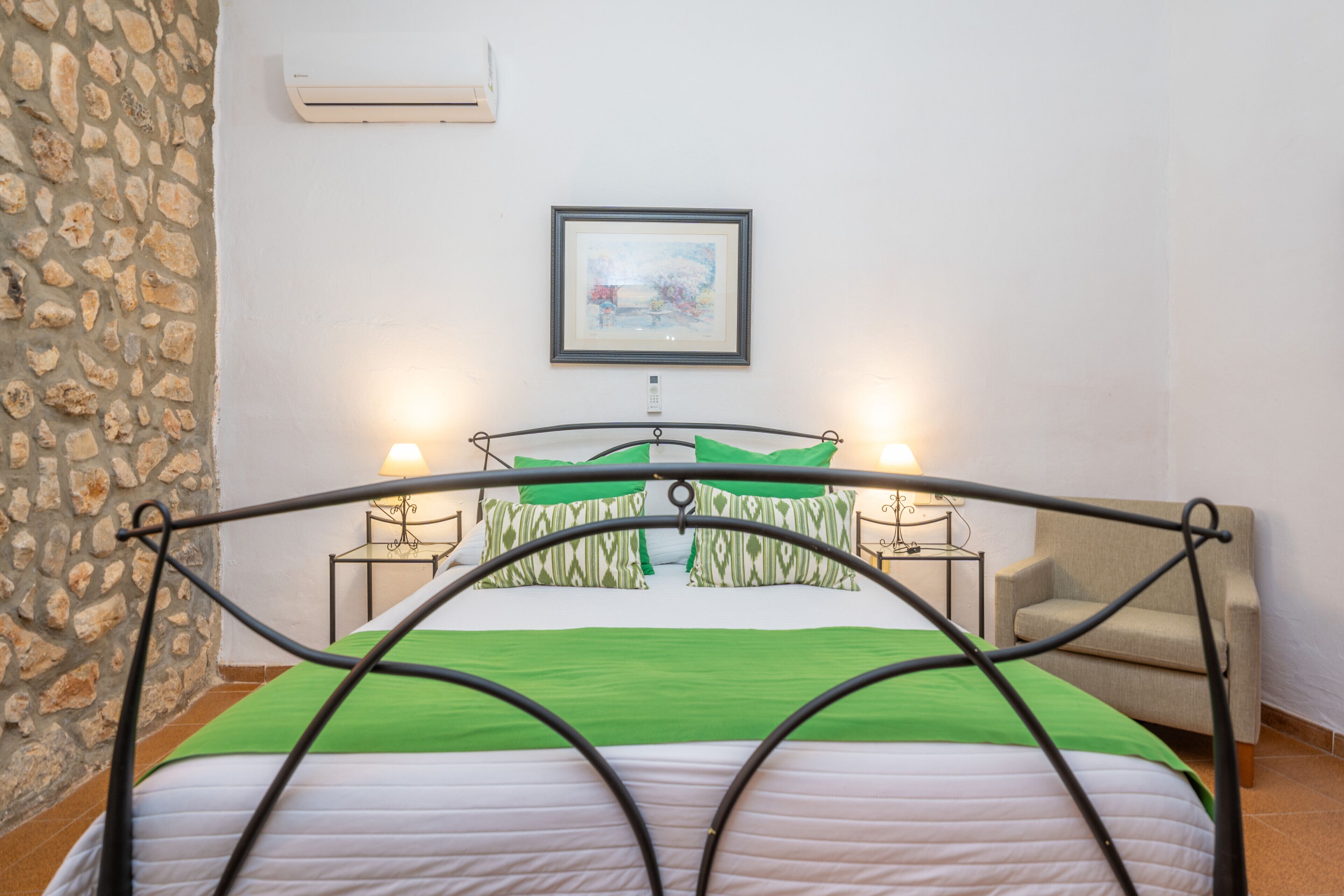 A bed with a metal frame, a green bedspread, and two bedside lamps. There is a framed picture on the wall above the bed.
